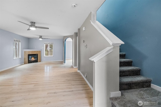 unfurnished living room featuring baseboards, stairway, a fireplace, light wood-style floors, and a ceiling fan