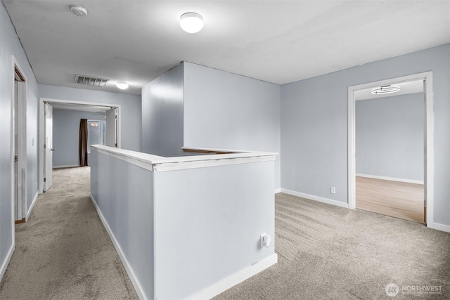 hall with an upstairs landing, visible vents, light carpet, and baseboards