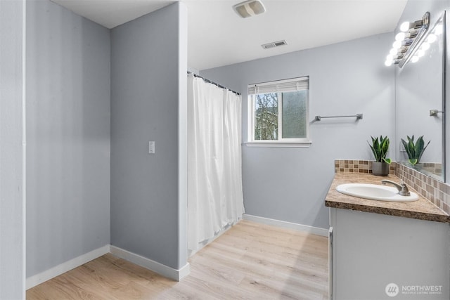 bathroom with tasteful backsplash, visible vents, baseboards, wood finished floors, and vanity