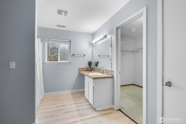 bathroom with vanity, wood finished floors, visible vents, baseboards, and tasteful backsplash