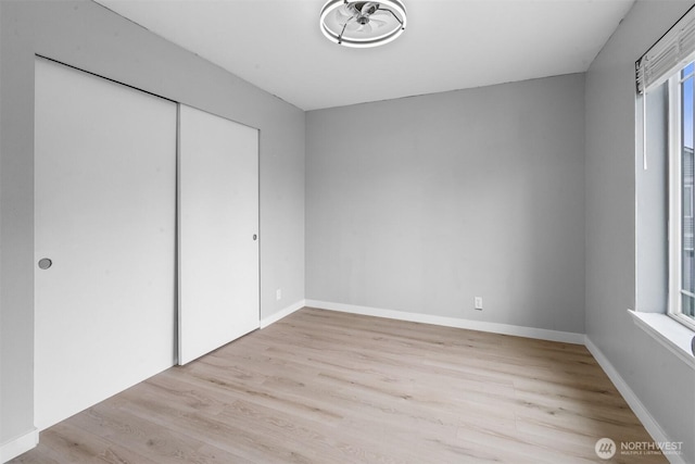 unfurnished bedroom with light wood-style flooring, multiple windows, baseboards, and a closet