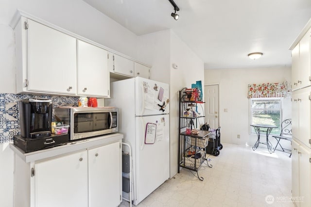 kitchen with stainless steel microwave, light floors, white cabinetry, and freestanding refrigerator