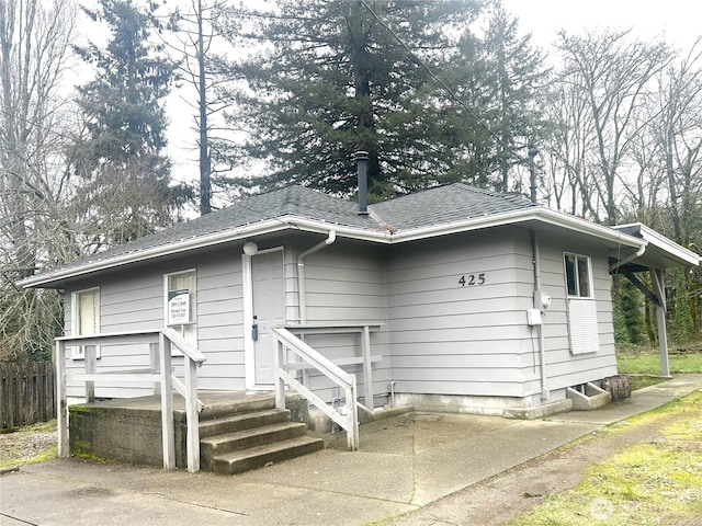 view of front of property with concrete driveway, fence, and a shingled roof