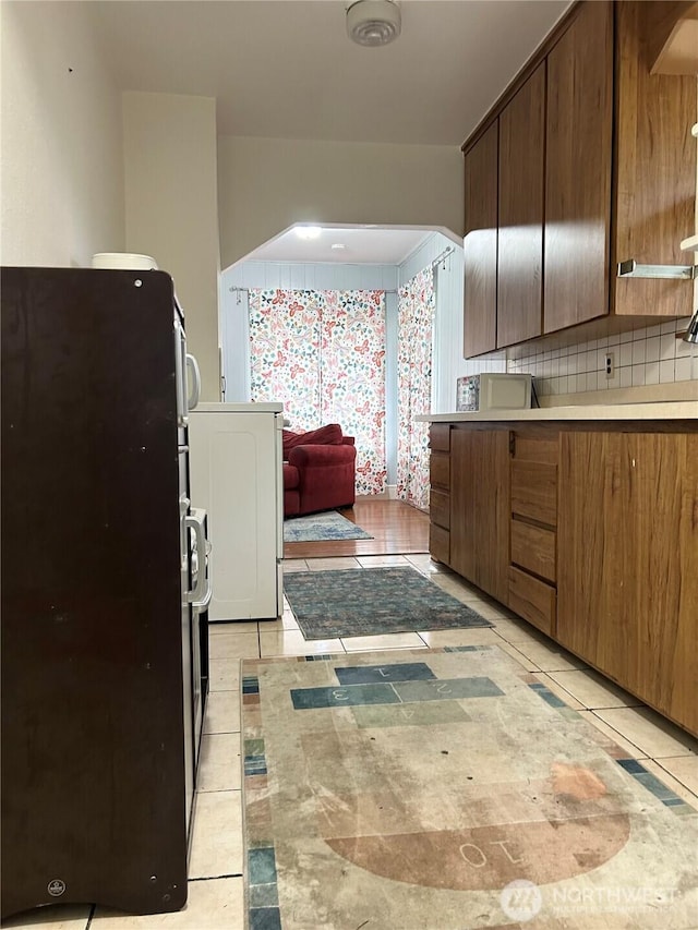 kitchen with backsplash, light countertops, light tile patterned flooring, arched walkways, and refrigerator