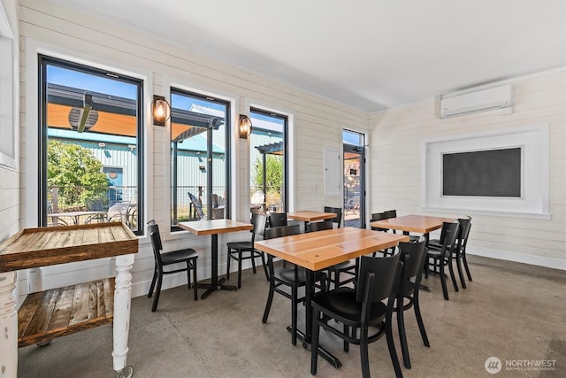 dining space with concrete floors, a healthy amount of sunlight, a wall mounted AC, and baseboards