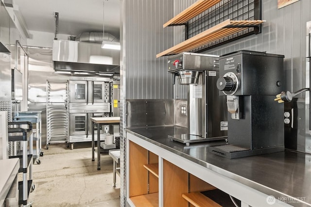 kitchen with open shelves, stainless steel countertops, brown cabinets, and concrete flooring