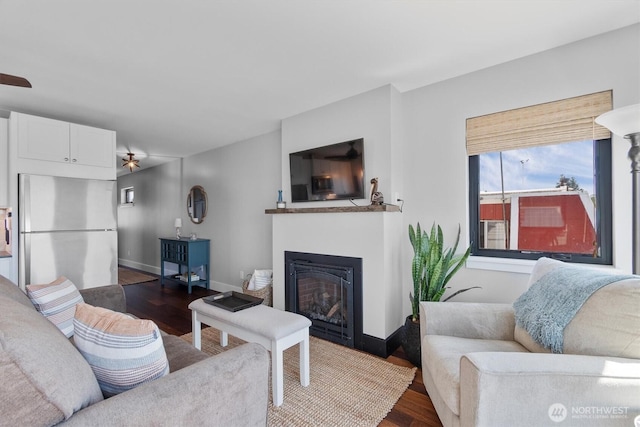 living room featuring ceiling fan, a fireplace, dark wood-style flooring, and baseboards