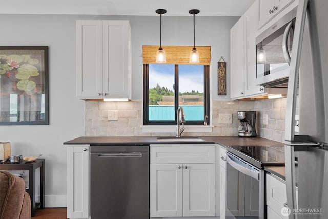 kitchen with dark countertops, white cabinets, appliances with stainless steel finishes, and a sink