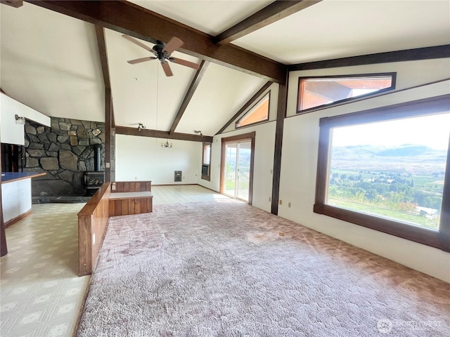 unfurnished living room with a stone fireplace, vaulted ceiling with beams, a ceiling fan, and carpet flooring