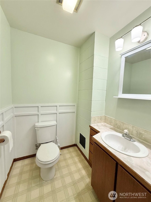 half bath with tile patterned floors, vanity, toilet, and wainscoting