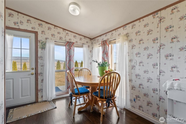 dining area featuring wallpapered walls, crown molding, baseboards, dark wood finished floors, and lofted ceiling