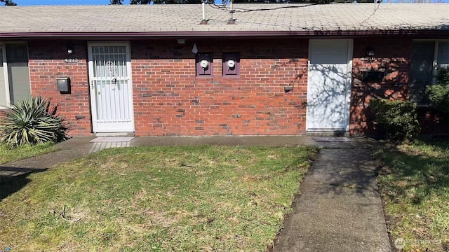 doorway to property featuring a yard and brick siding