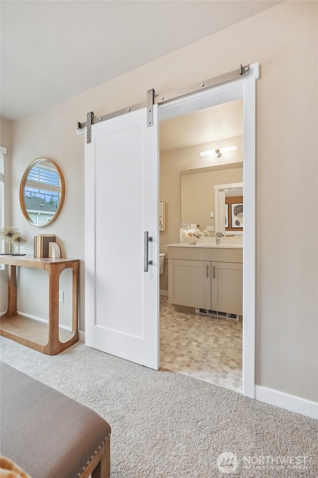 interior space featuring a barn door, carpet floors, baseboards, and connected bathroom