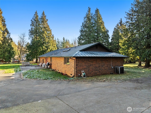 view of side of property with a standing seam roof, a lawn, brick siding, and metal roof