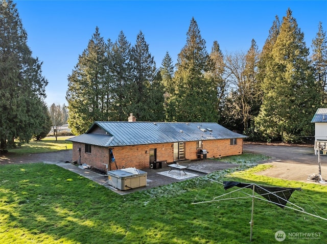 back of property with a patio, a standing seam roof, a yard, brick siding, and metal roof