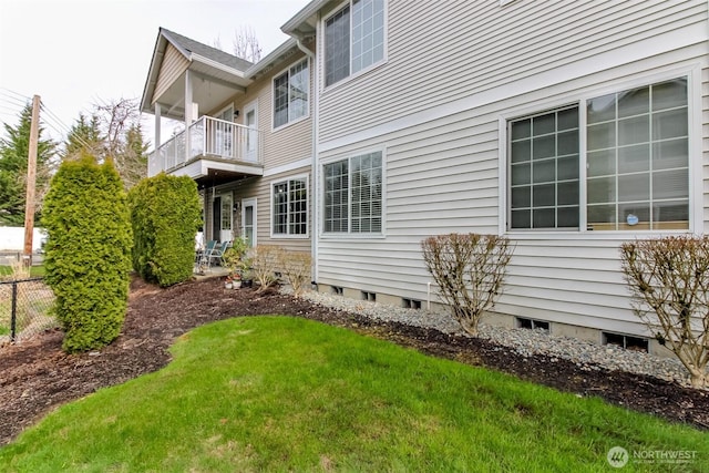 view of side of home with a balcony, fence, a lawn, and crawl space