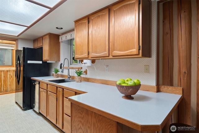 kitchen featuring wallpapered walls, a peninsula, a sink, light countertops, and stainless steel dishwasher