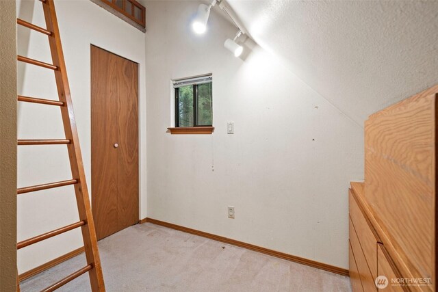 interior space featuring light carpet, track lighting, a textured ceiling, baseboards, and vaulted ceiling