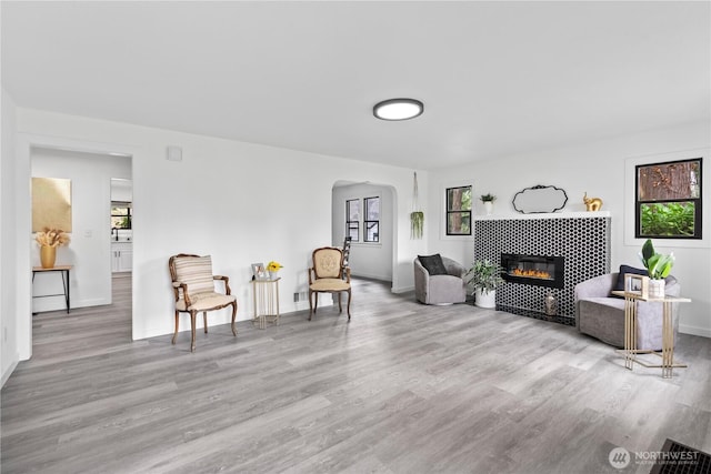 living area with baseboards, arched walkways, wood finished floors, and a fireplace