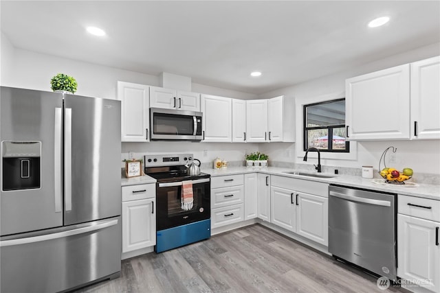 kitchen with light countertops, light wood-style flooring, appliances with stainless steel finishes, white cabinets, and a sink