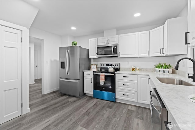 kitchen with wood finished floors, appliances with stainless steel finishes, white cabinetry, and a sink