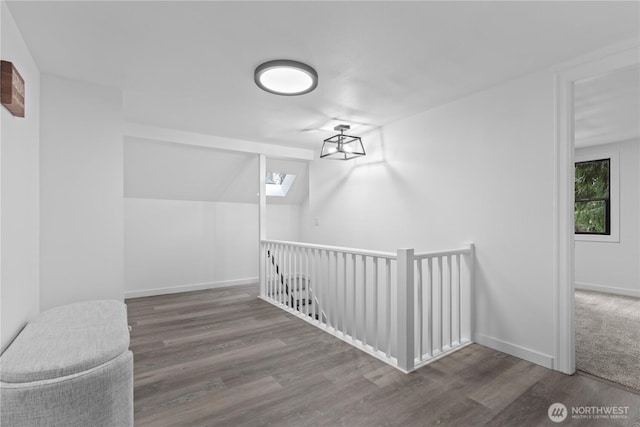 hall with an upstairs landing, a skylight, baseboards, and wood finished floors