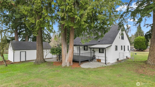 rear view of property featuring a shingled roof, fence, a wooden deck, a lawn, and an outdoor structure