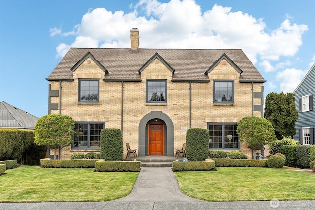 view of front of property featuring a front yard, brick siding, and a chimney