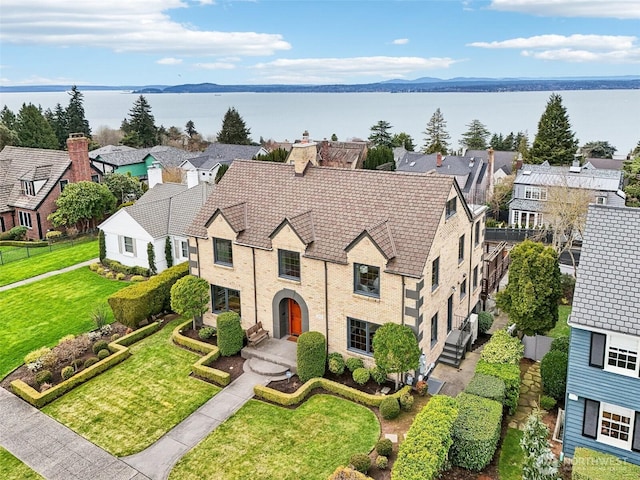 view of front of home featuring a water view, a front lawn, a residential view, brick siding, and a chimney