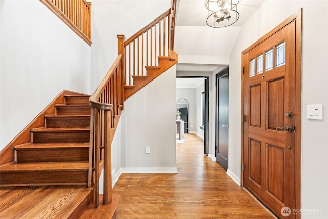 foyer with a notable chandelier, lofted ceiling, wood finished floors, baseboards, and stairs