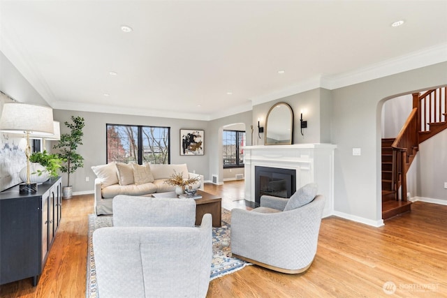 living room featuring stairs, a glass covered fireplace, arched walkways, and light wood-type flooring