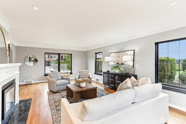 living room featuring light wood-type flooring, a high end fireplace, and crown molding