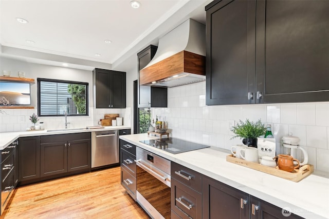 kitchen featuring light countertops, light wood-style flooring, custom exhaust hood, stainless steel appliances, and a sink