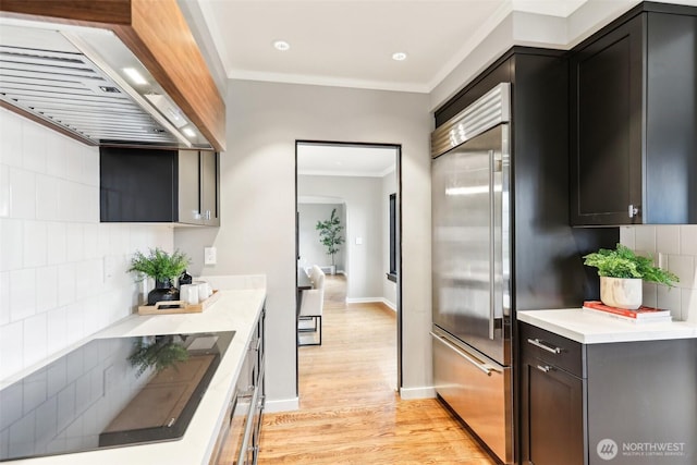 kitchen with light wood-style flooring, ornamental molding, built in fridge, wall chimney exhaust hood, and black electric cooktop