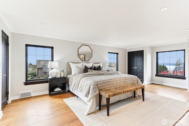 bedroom with light wood finished floors, visible vents, multiple windows, and baseboards