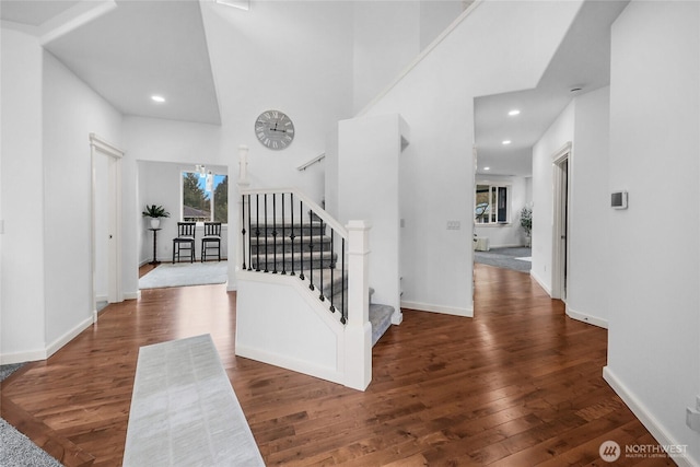 hallway featuring hardwood / wood-style floors, baseboards, and a towering ceiling