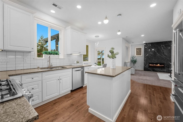 kitchen featuring a healthy amount of sunlight, dishwasher, a premium fireplace, wood finished floors, and a sink