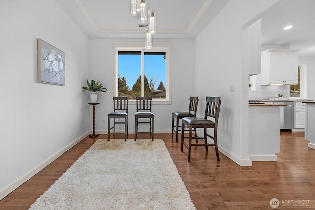 living area featuring a tray ceiling, baseboards, and wood finished floors