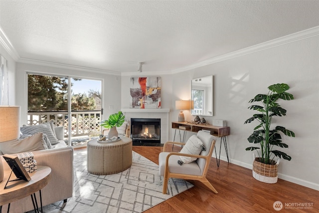 living area with wood finished floors, baseboards, ornamental molding, a textured ceiling, and a tiled fireplace