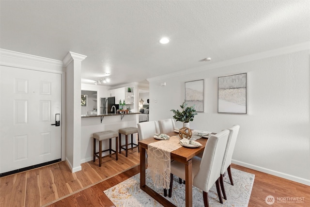 dining room featuring light wood-type flooring, baseboards, a textured ceiling, and ornamental molding