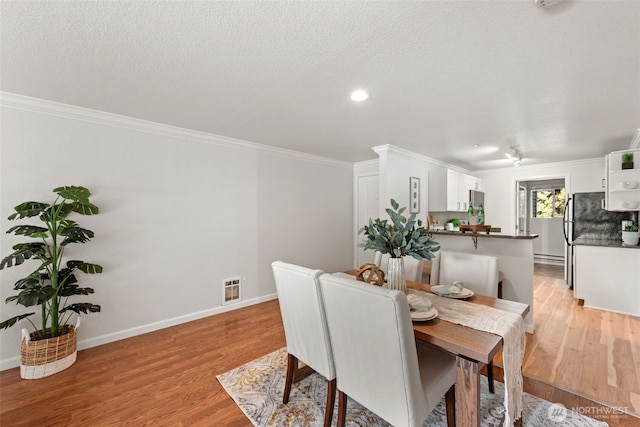 dining space featuring visible vents, a textured ceiling, light wood-type flooring, and ornamental molding