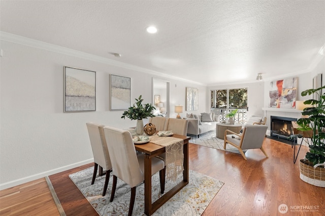 dining space with a textured ceiling, a warm lit fireplace, wood finished floors, and crown molding