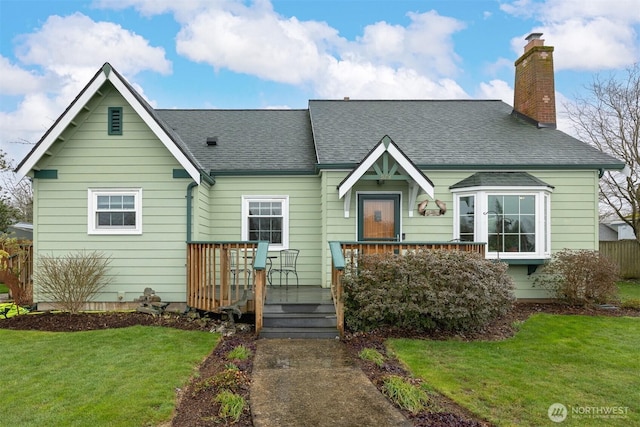 view of front of home featuring roof with shingles, a chimney, a deck, and a front lawn