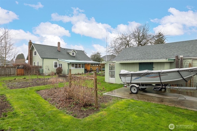 rear view of house with fence, roof with shingles, a yard, a chimney, and concrete driveway