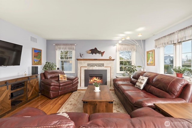 living area featuring wood finished floors, a healthy amount of sunlight, visible vents, and a tile fireplace