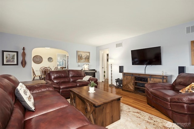 living area featuring light wood-style floors, arched walkways, and visible vents