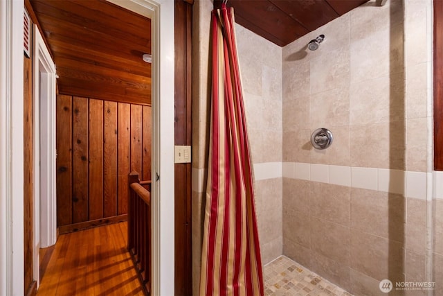 bathroom featuring wood finished floors, wooden walls, wood ceiling, and tiled shower