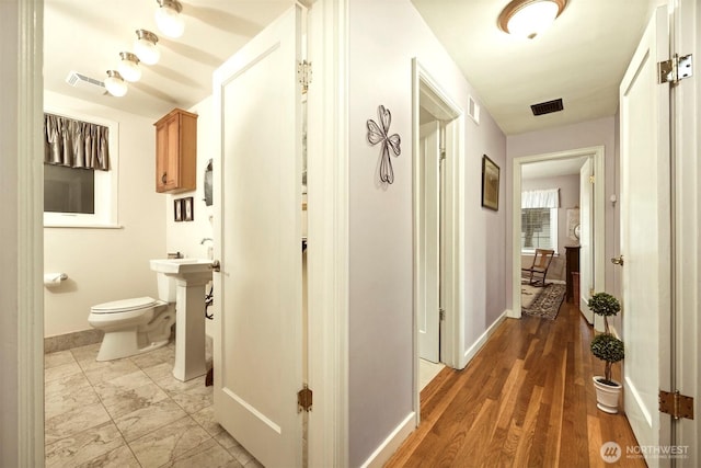 hallway with baseboards, visible vents, and marble finish floor