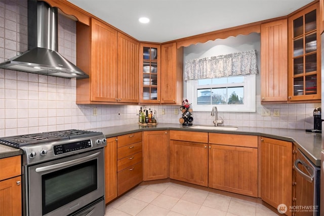 kitchen with dark countertops, wall chimney range hood, decorative backsplash, stainless steel gas stove, and a sink