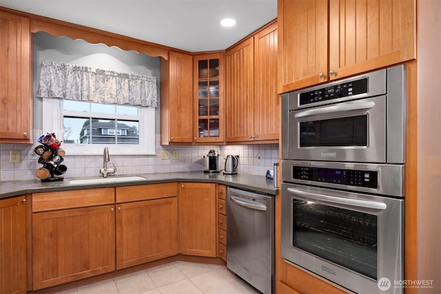 kitchen featuring light tile patterned floors, a sink, stainless steel appliances, glass insert cabinets, and backsplash